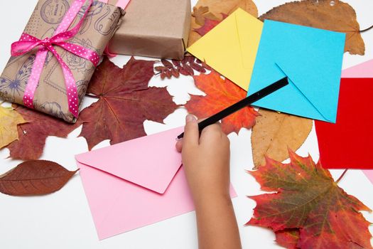 children's hand writes on an envelope on a white table, postcards, envelopes, Thanksgiving, birthday, holiday, congratulations, autumn leaves on the background, copy space