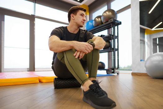 The man is massaging his leg muscles with the foam roller in gym