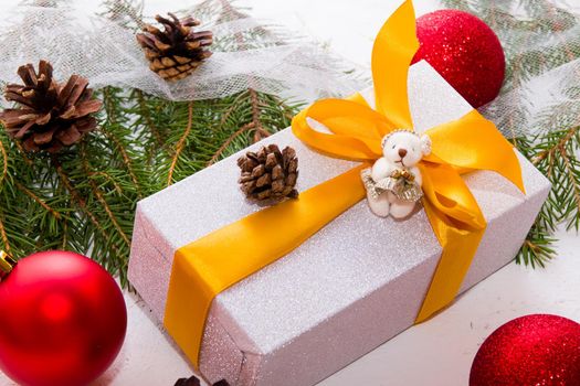 gift box in wrapping paper with a gold ribbon on the background of fir branches and balls, Christmas, New Year 2020