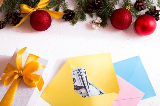 money in an envelope, gift box with a golden bow and Christmas ornaments on a white background, Christmas toys, cones, fir branches, frame