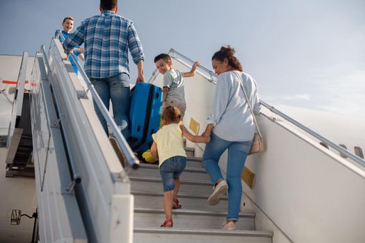 Back view of parents with two kids getting on, boarding the plane on a daytime, ready for summer vacations. People, traveling, vacation concept