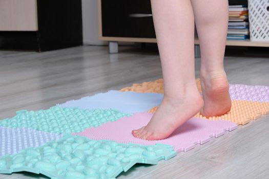 the child walks on the mat for massage of the feet at home. Prevention of flat feet and hallux valgus Orthopedic massage puzzle mats for the development of children.