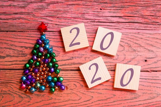 tree made of beads and shiny bells, wooden squares for your new year date, red wooden background 2020 text date