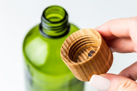 Green glass cosmetic bottle with wooden cover for beauty products refill. Minimalistic plastic free bathroom accessories