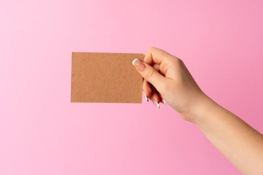 Woman hand showing blank business card on pink background. Close up.