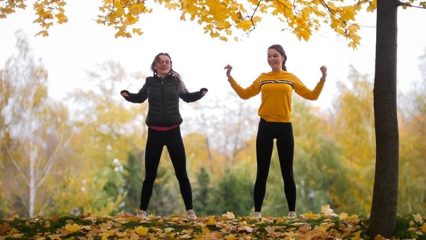 Acrobatic girls in jackets warming up outside before training in park. Hands to the sides. Autumn. Fall
