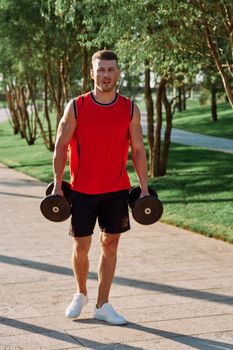 athletic man with dumbbells in his hands outdoors in the park. High quality photo