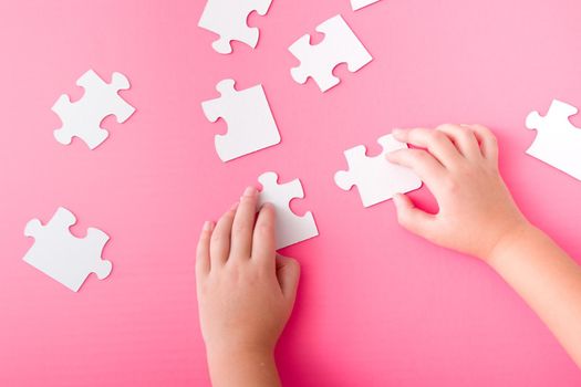 children's hands stack paper white puzzle on pink background