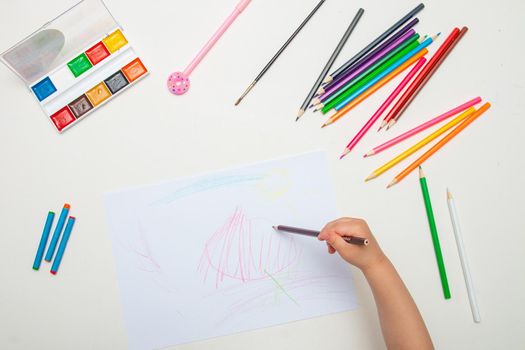 child draws with crayons on white lsita on a white table top view copy space