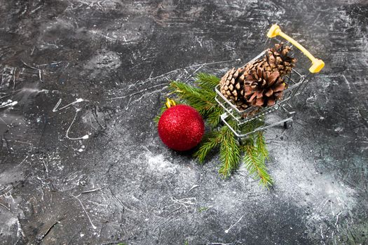 Christmas shopping, online shopping, shopping cart with pine cones and Christmas red ball, spruce branch, black background, copy space