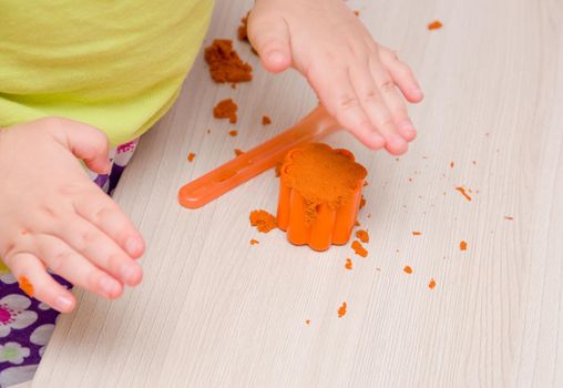 children's hand presses orange sand in a mold for toy muffins and cakes on a beige wooden table