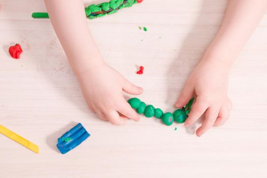 a small child sculpts a caterpillar from green plasticine on a wooden table, the development of fine motor skills of hands, what to do with the child at home, stay at home