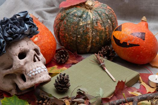 ceramic skull in a wreath of flowers from black ribbons, cones, autumn leaves, a candle and pumpkins, a jack head, a witch book, blurred background, halloween background