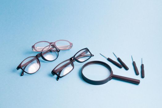 a magnifier, several pairs of glasses and small screwdrivers are on a blue background, children's glasses and glasses for adults are being repaired