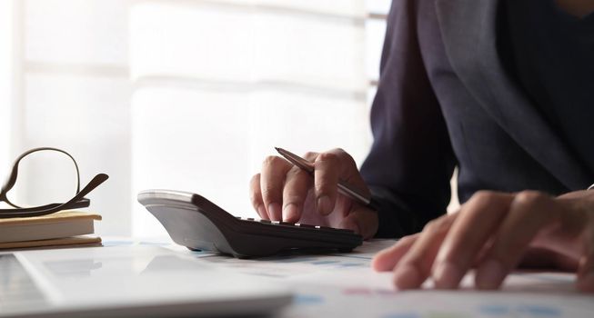 Close up of businessman or accountant hand holding pen working on calculator to calculate business data, accountancy document and laptop computer at office, business concept.