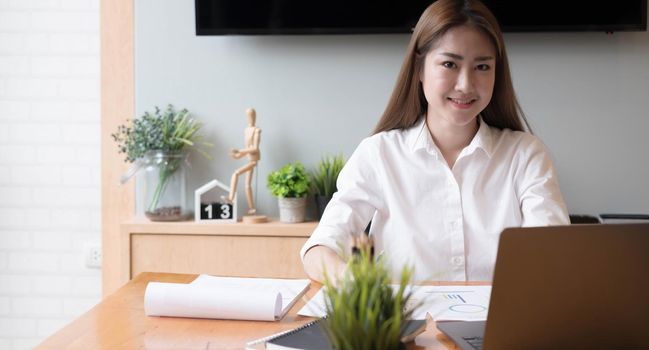 Portrait of Young Asian woman freelancer is working her job on computer tablet in modern office. Doing accounting analysis report real estate investment data, Financial and tax systems concept.