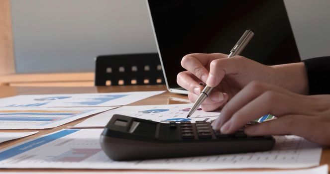 Close up Hands of businesswoman or accountant holding pen and working on calculator to calculate business data, Accountancy document and laptop computer at office, Business concept.