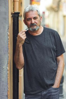 Mature man looking at camera in urban background. Senior male with white hair and beard wearing casual clothes.