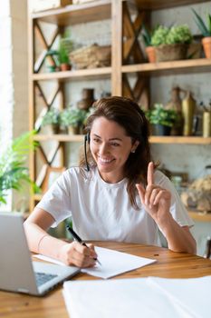 Smiling woman working at home in front of a laptop monitor. She held up her finger to indicate the importance of the idea. Modern technology concept.