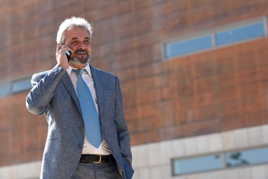 Portrait of a senior businessman talking with a smart phone outside of modern office building. Successful business man in urban background.