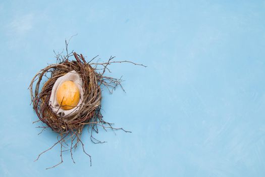 golden easter egg in a makeshift nest on a blue background copy space top view