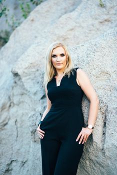 blonde girl in a black trouser suit with blue eyes on the background of a granite quarry from gray rubble