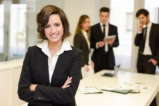 Businesswoman leader looking at camera in working environment. Young woman wearing black blazer jacket