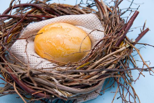golden easter egg in a makeshift nest of twigs on a blue background close-up