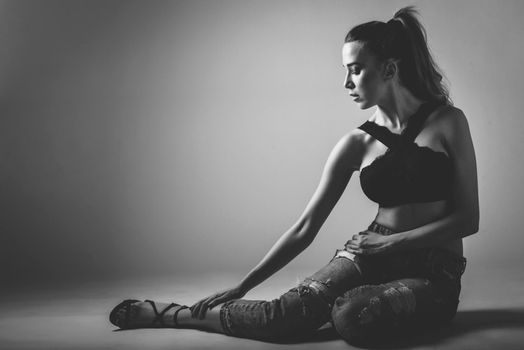 Beautiful caucasian woman with very long hair wearing black bra and blue jeans sitting on white floor. Wavy hairstyle. Studio shot.