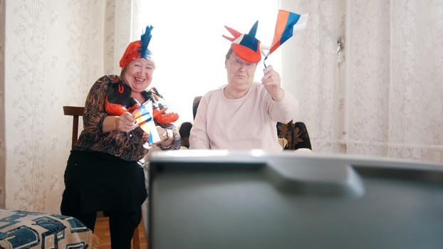 Two elderly women watching in russian accessories TV. Having fun. Portrait