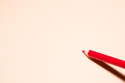 One red pencil on a light orange background with a dark shadow.