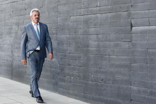 Senior businessman walking outside of modern office building. Successful business man wearing suit and tie in urban background.