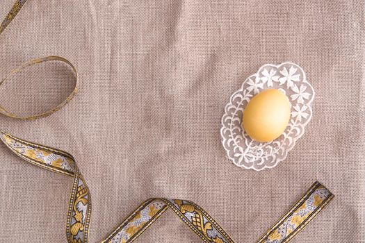 easter yellow egg on lace, gold lace, linen fabric background, copy space, top view, frame, easter backgroun