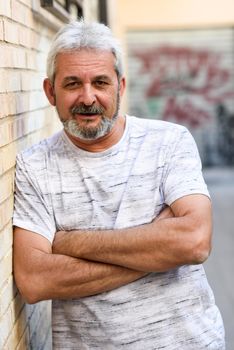 Mature man smiling at camera in urban background. Senior male with white hair and beard wearing casual clothes.