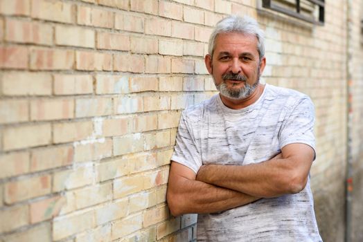 Mature man smiling at camera in urban background. Senior male with white hair and beard wearing casual clothes.