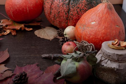 a jar of tea, autumn fruits and vegetables, dry apples, a branch, autumn leaves, a cold treatment in the fall, orange flowers, copy space, autumn mood, Halloween, well-being day, seasonal theme, winter harvest,brown wooden table background