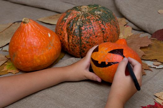 the child draws a pumpkin face on a black market, jack o lantern, halloween background, preparation for the holiday