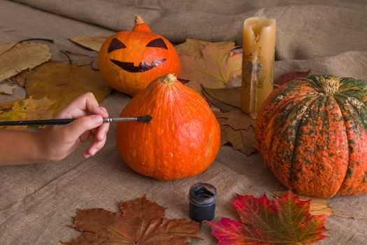 children's hand draws with a brush on a pumpkin black paint. preparation for halloween, holiday, atmosphere halloween