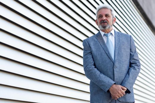 Portrait of a senior businessman with arms crossed outside of modern office building. Successful business man in formal smiling in urban background.