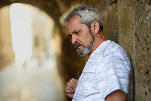 Portrait of a mature serious man in urban background. Senior male with white hair and beard wearing casual clothes.