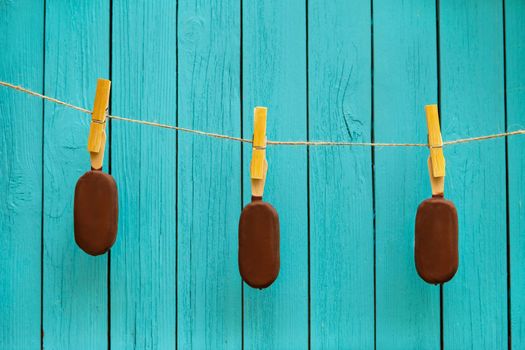 three tasty chocolate ice cream on rope near turquoise background. summer food concept