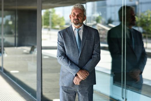 Portrait of a senior businessman with arms crossed outside of modern office building. Successful business man in formal smiling in urban background.