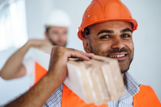 Two young men builders carrying wood planks on construction site, close up photo