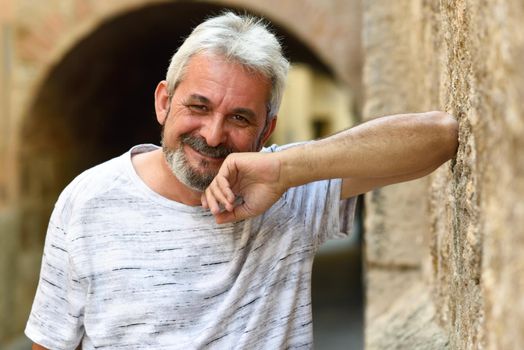 Mature man smiling at camera in urban background. Senior male with white hair and beard wearing casual clothes.