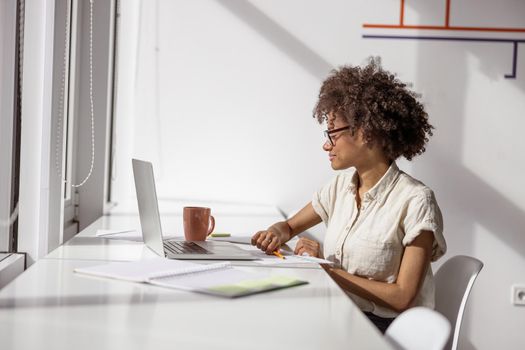 Pretty woman in glasses making notes while sitting at her workplace near the window