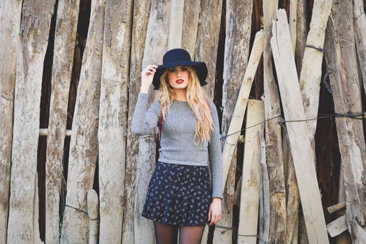 Beautiful young blonde woman, model of fashion, in rural background. Girl wearing sweater, skirt and hat.