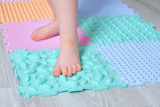 the child walks on the mat for massage of the feet at home. Prevention of flat feet and hallux valgus Orthopedic massage puzzle mats for the development of children.
