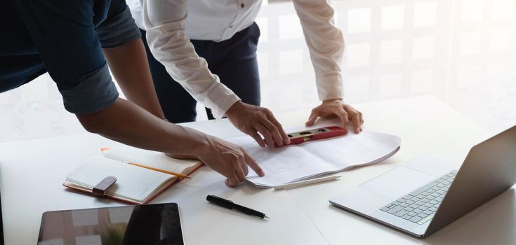 Two construction engineers working at construction site with blueprint on table.