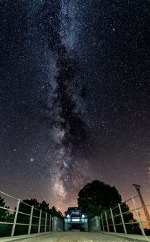 Night shot of 4x4 car and narrow bridge under the milky way, vertical composition
