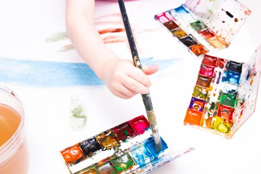 the child draws with a brush with watercolors on a white sheet, a table, a copy place